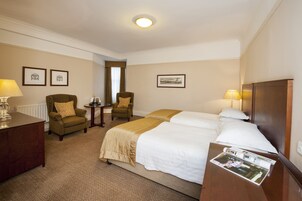 A hotel room with two beds, a desk, two armchairs, and a small table.