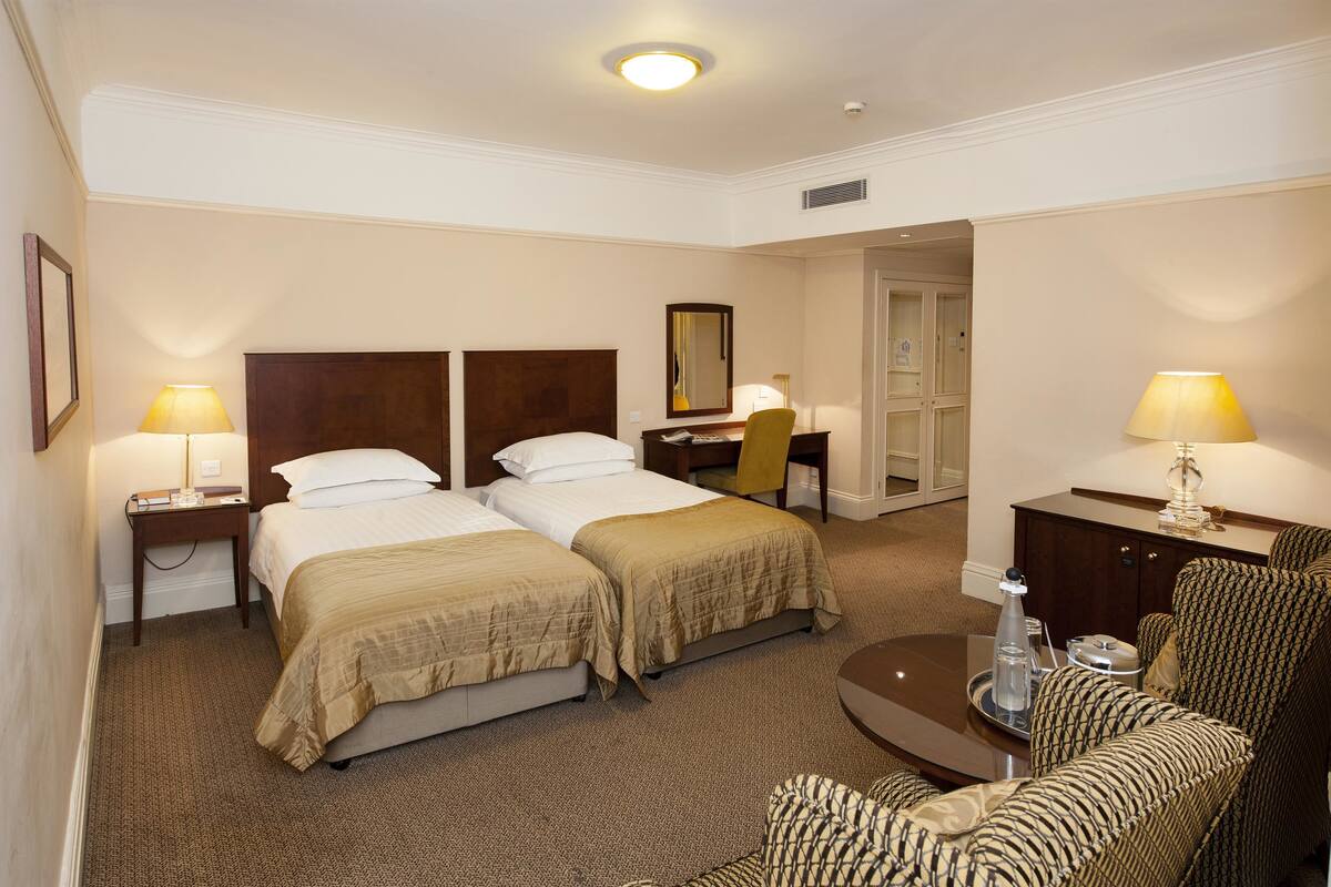 Une chambre d’hôtel avec deux lits, un bureau, une chaise, un canapé et une petite table avec un plateau.
