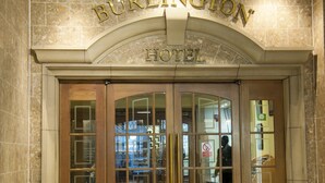 La entrada del Hotel Burlington, con un diseño clásico, presenta grandes puertas de cristal y un arco prominente.