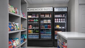 A hotel room with a kitchenette area featuring shelves stocked with snacks, beverages, and packaged foods.