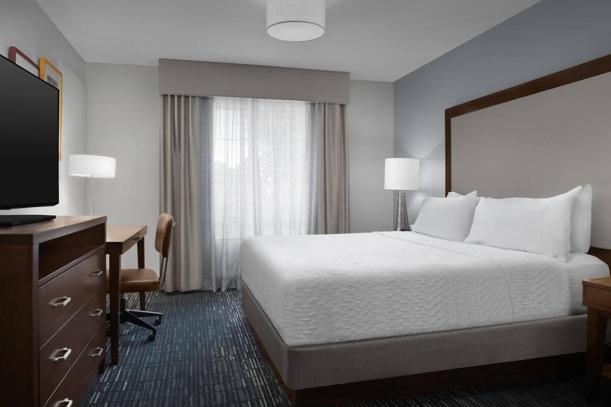 Hotelkamer met een groot bed, een bureau, een stoel, een televisie en een raam met gordijnen.