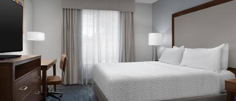 A hotel room with a large bed, a desk, a chair, a TV, and a window with curtains.