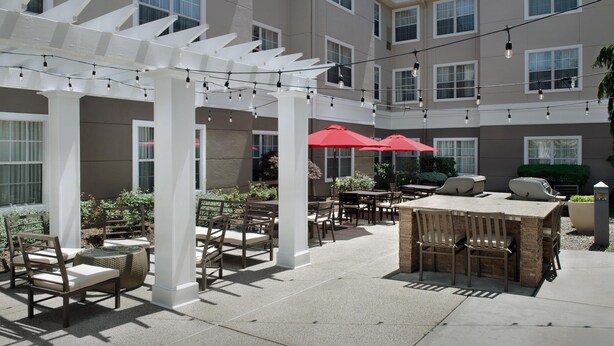 An outdoor patio area with tables and chairs, string lights, and red umbrellas.