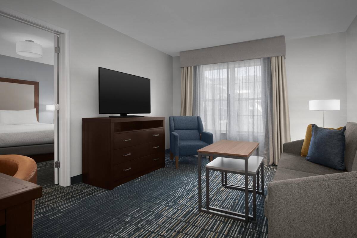 Hotelkamer met een bed, televisie, bureau, stoel, bank en raam met gordijnen.