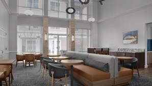 A modern lounge area with a sectional sofa, round tables, and chairs, featuring a patterned carpet and large windows.