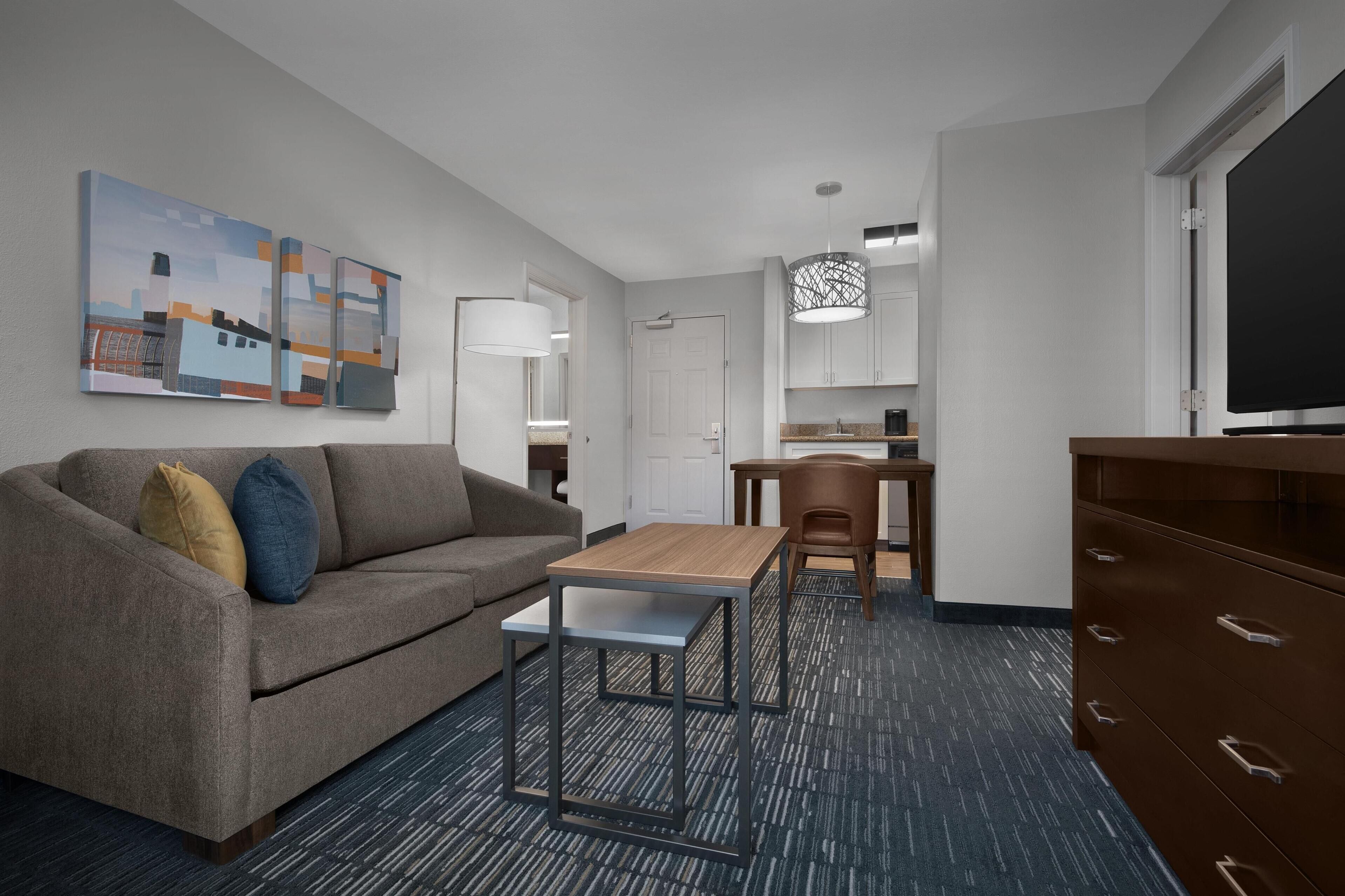 Een moderne hotelkamer met een bank, een tafeltje, een televisie, een bureau en een kitchenette.
