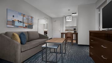 Een moderne hotelkamer met een bank, een tafeltje, een televisie, een bureau en een kitchenette.