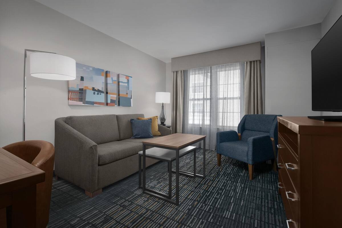 Een hotelkamer met een bank, een kleine tafel, een televisie en een lamp.