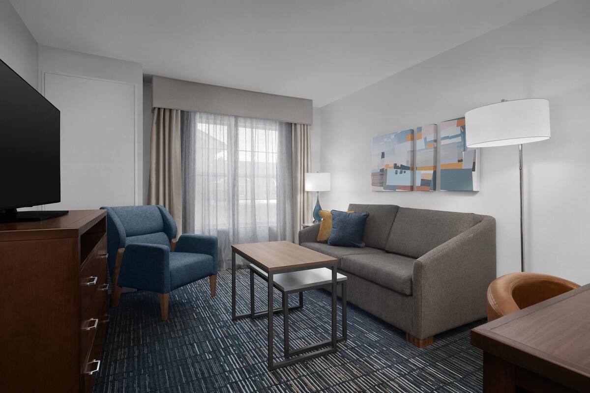 Een hotelkamer met een bank, twee fauteuils, een tafeltje, een televisie en een lamp.
