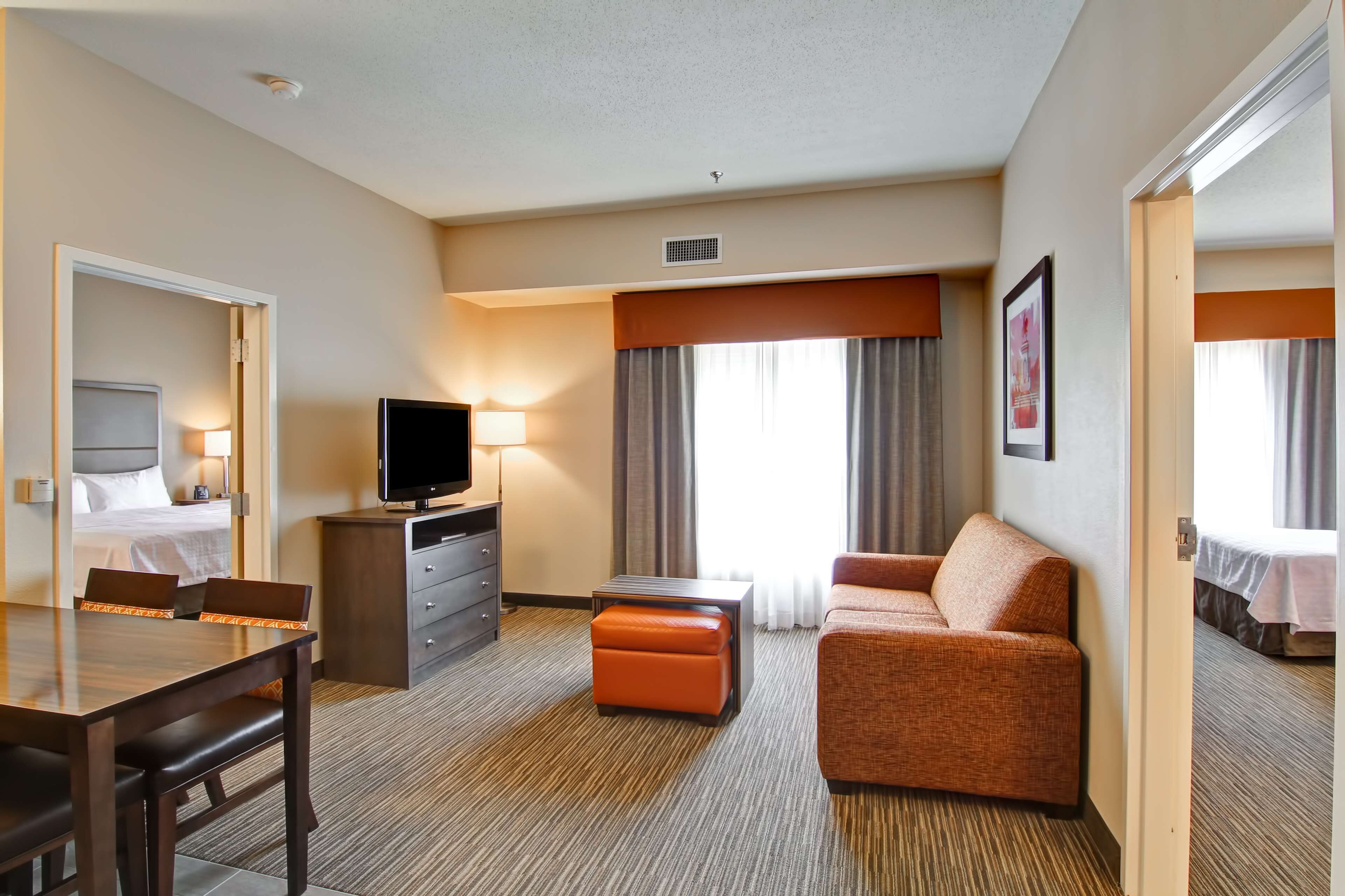 A hotel room with a bed, a TV, a desk with chairs, a sofa, and a window with curtains.