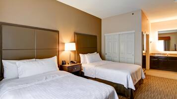 A hotel room with two beds, a bedside table with a lamp, a wardrobe, and a bathroom visible through an open door.
