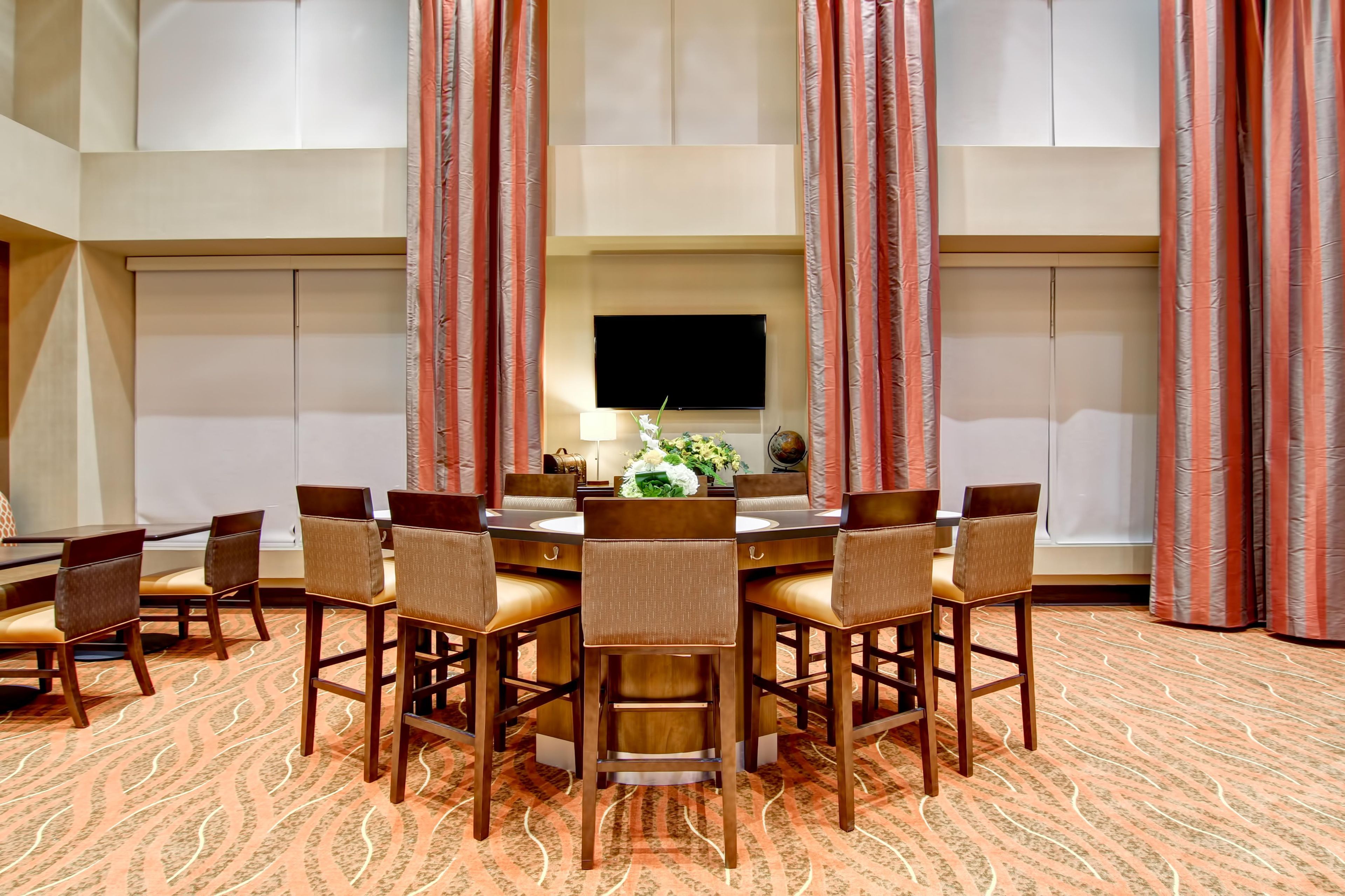 A conference room with a round table, chairs, a flat-screen TV, and a floral arrangement.