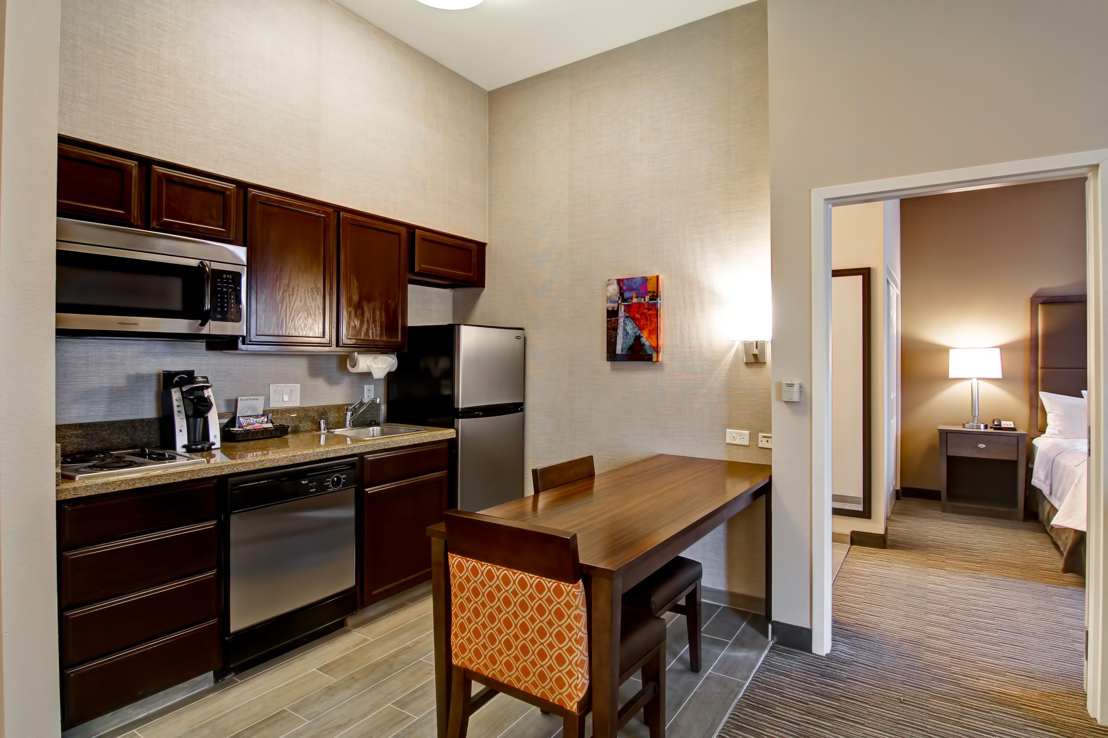 A compact hotel kitchen with modern appliances, a dining area, and a connecting bedroom.