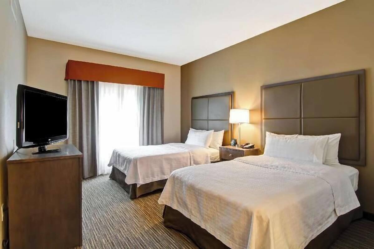 Une chambre d’hôtel avec deux lits, une télévision, une table de chevet et une fenêtre avec des rideaux.