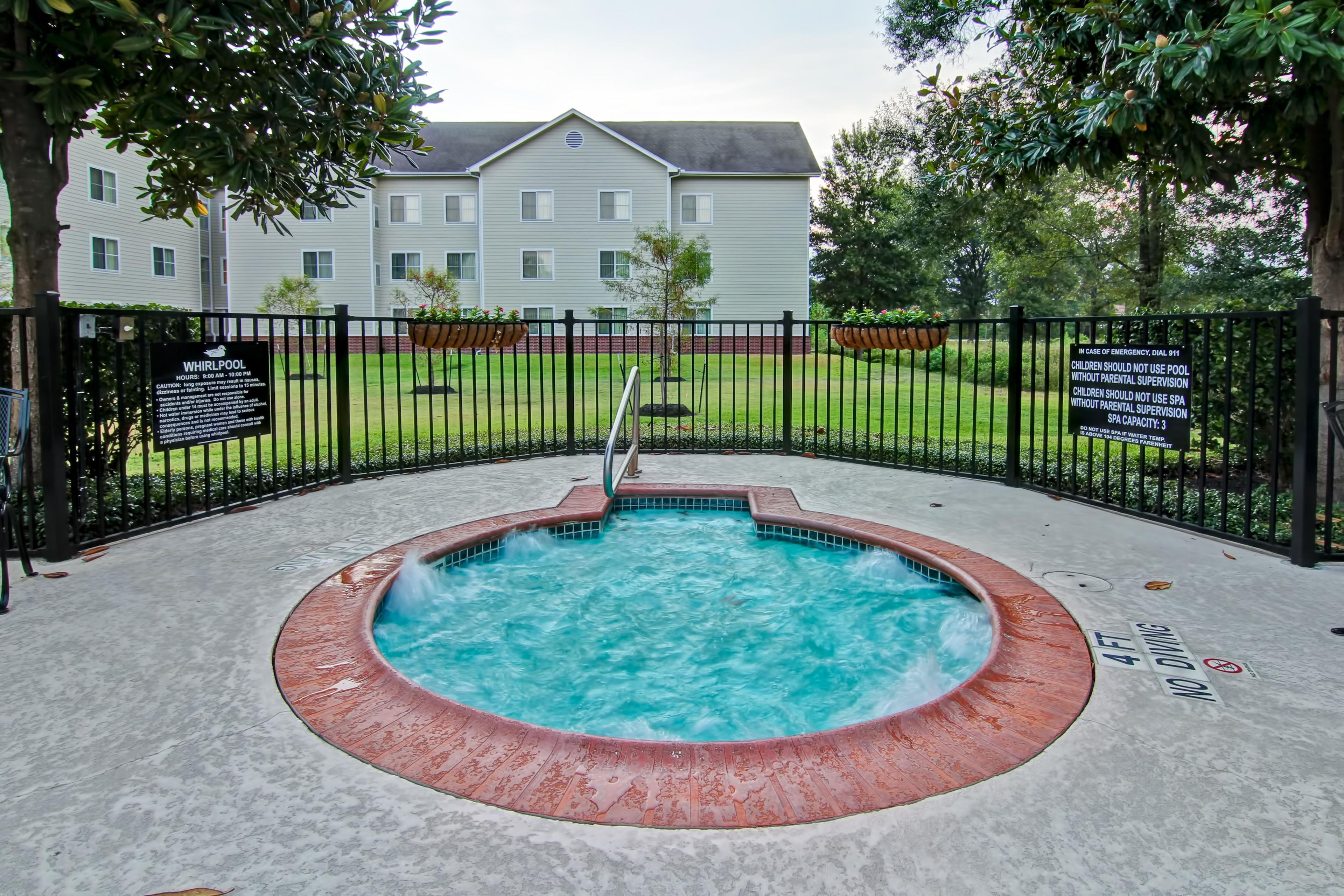 A hot tub surrounded by a fenced area with a building in the background.