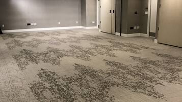 A large, empty conference room with a patterned carpet, recessed lighting, and a door on the right.
