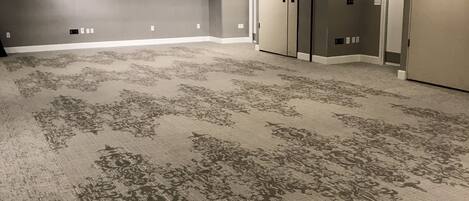 A large, empty conference room with a patterned carpet, recessed lighting, and a door on the right.