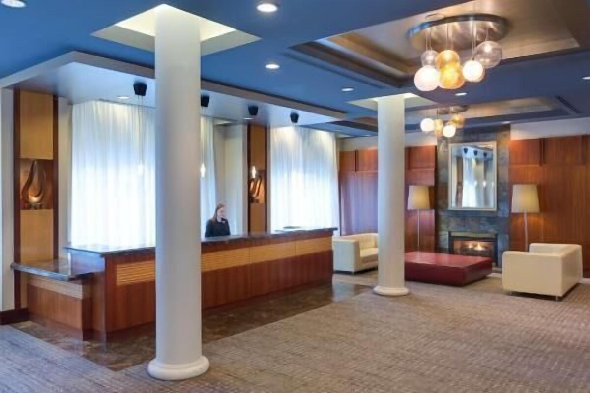 A hotel lobby with a reception desk, large white columns, a fireplace, and a chandelier.