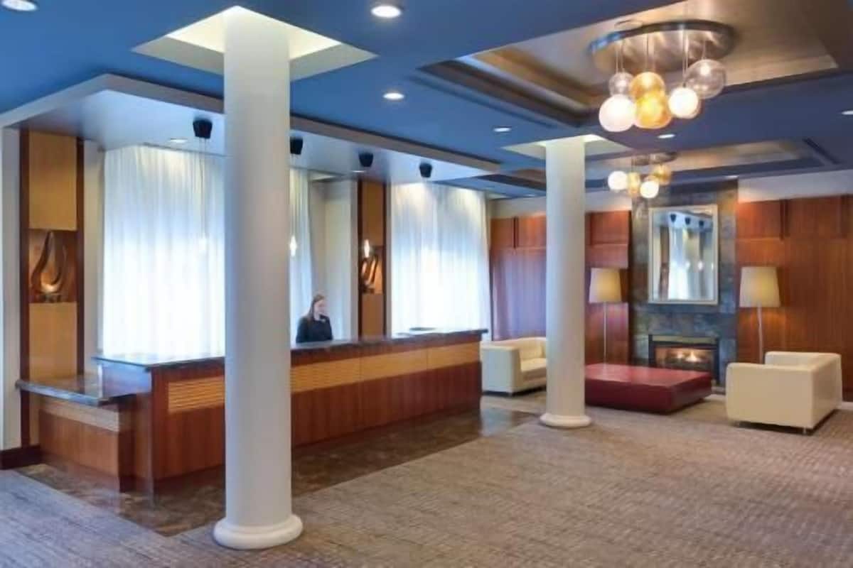 A hotel lobby with a reception desk, large white columns, a fireplace, and a chandelier.