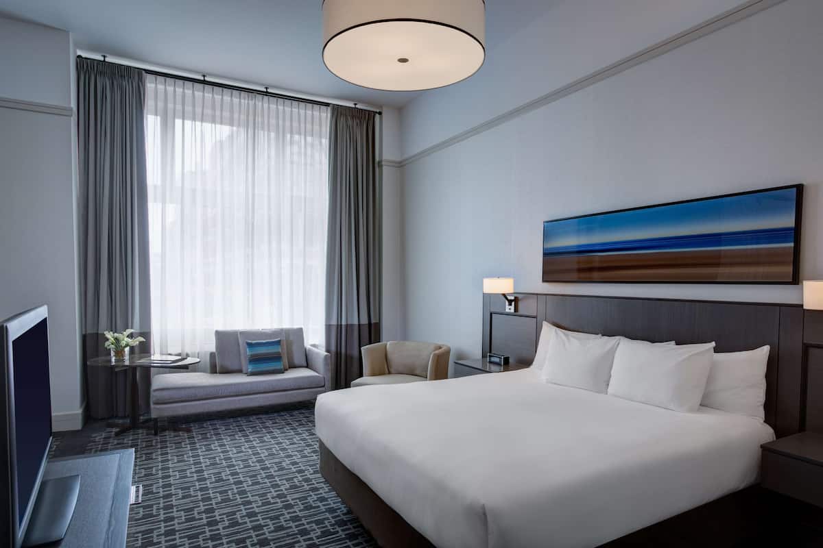 A hotel room with a large bed, a sofa, a TV, and a desk.