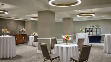 A hotel conference room with round tables, chairs, and a bar area with bottles.