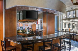 Zona de bar con una barra curva, varias opciones de asientos y una pantalla de televisión.