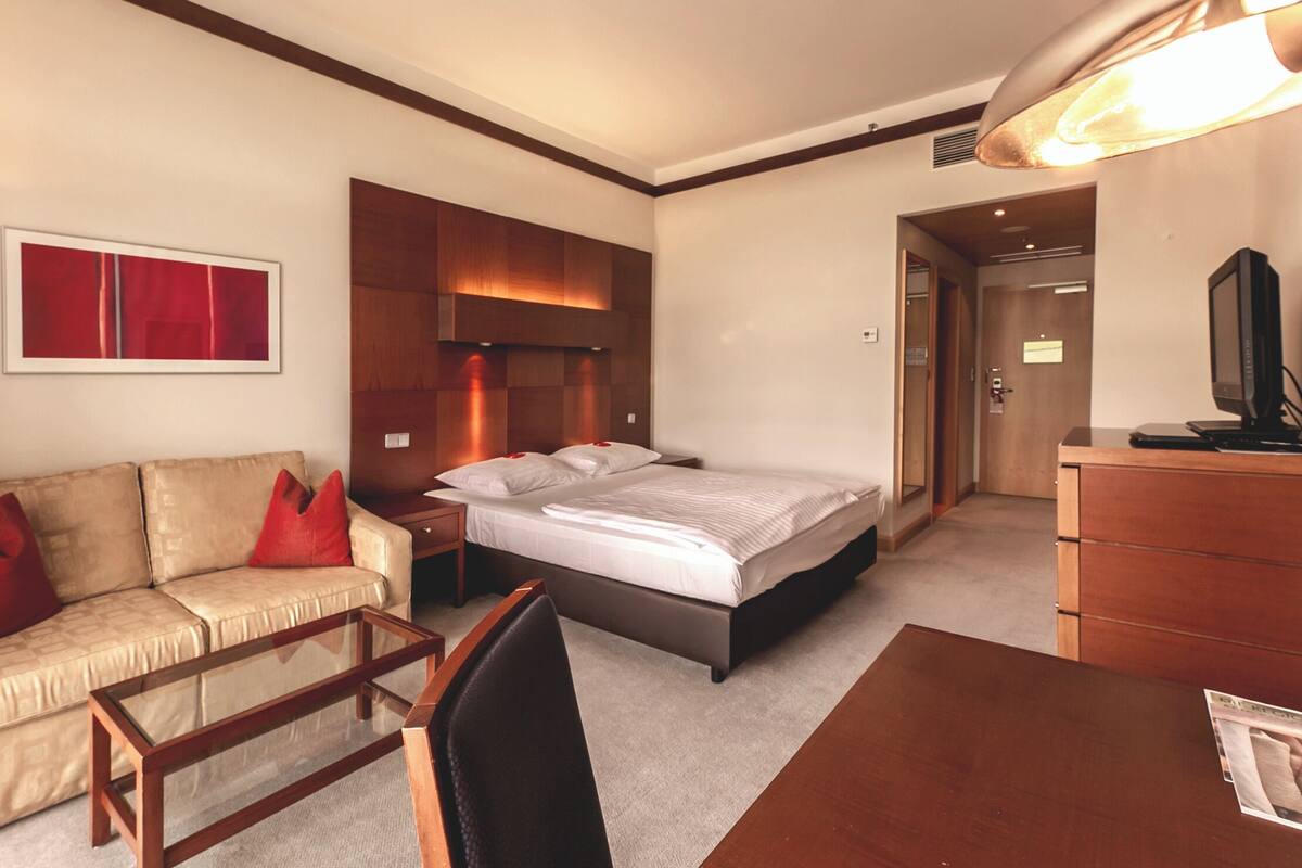 A hotel room with a bed, a sofa, a desk, and a television.
