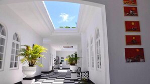 A corridor with a checkered floor, white walls, and a skylight. There are potted plants and artwork on the walls. - Jamaica Palace Hotel (Port Antonio)