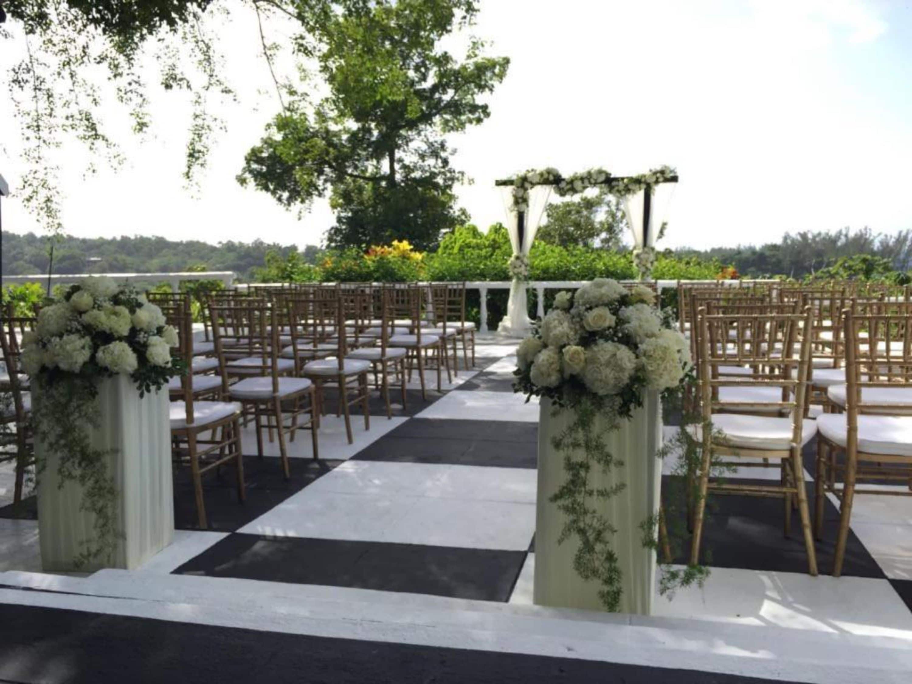 An outdoor venue with rows of wooden chairs and white cushions, arranged in a checkered pattern on the ground.