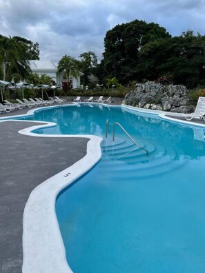 Relax by the pool surrounded by lounge chairs and umbrellas, with a natural rock formation in the background.