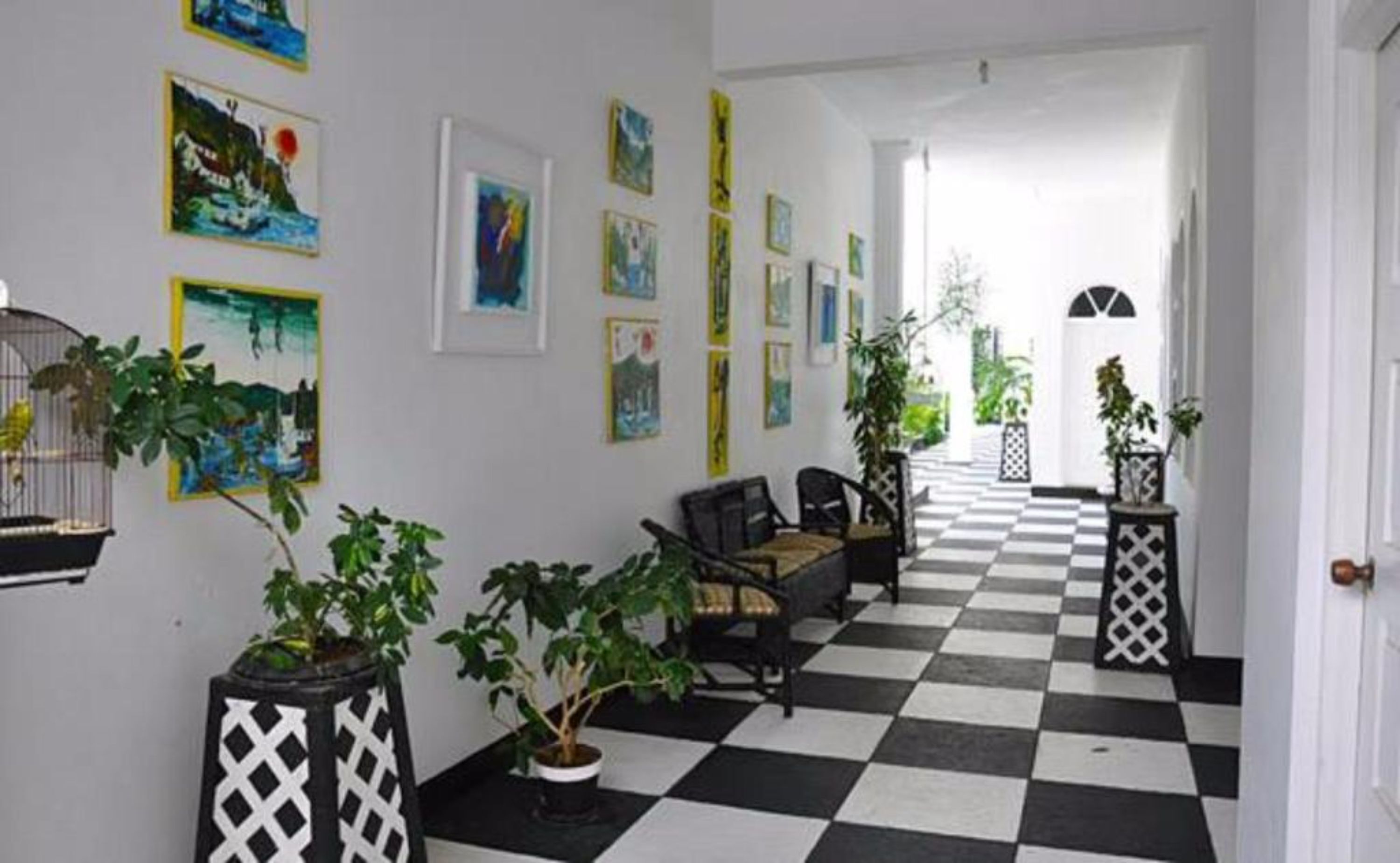 Un pasillo con piso de cuadros, obras de arte enmarcadas en las paredes y plantas en macetas.