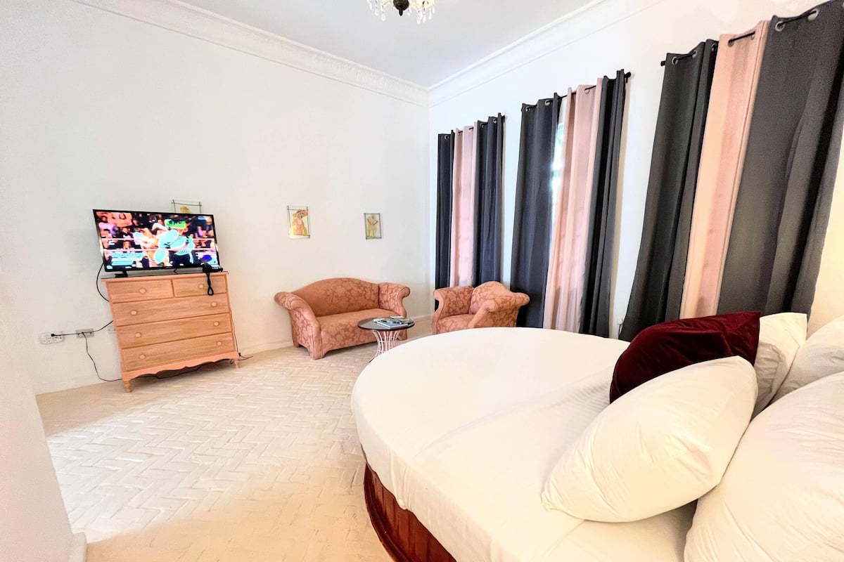 Une chambre d’hôtel avec un grand lit, deux fauteuils, une petite table, un téléviseur et une commode.