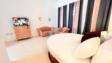 Une chambre d’hôtel avec un grand lit, deux fauteuils, une petite table, un téléviseur et une commode.