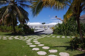 Stroll through the serene garden, lined with a meandering pathway and lush greenery, to reach the charming building with a thatched roof.