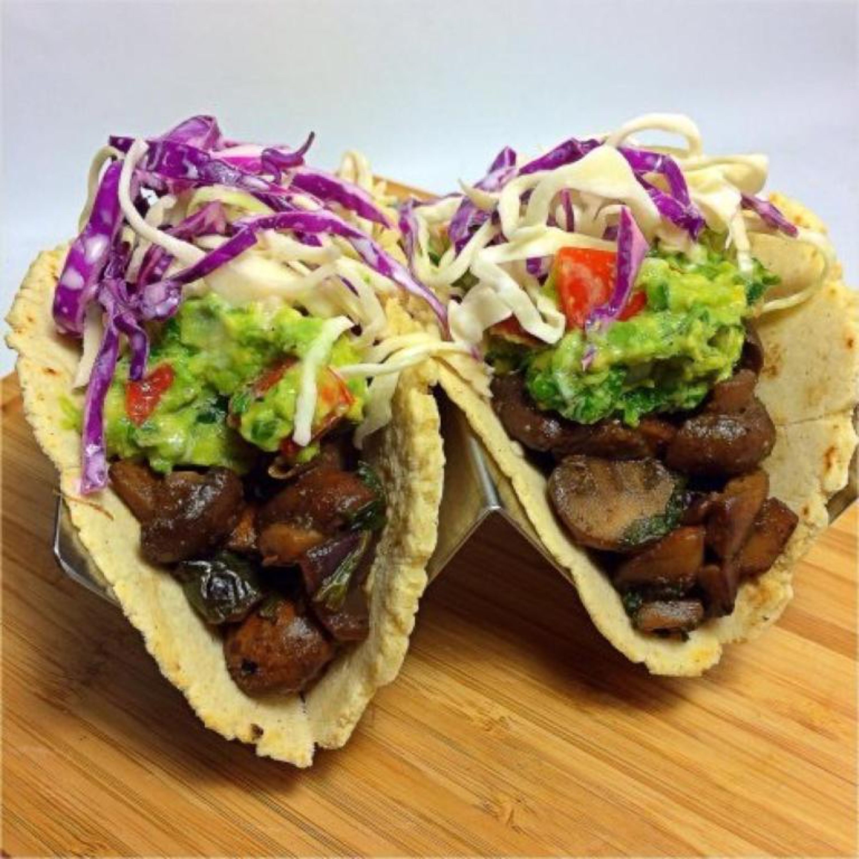 Two tacos with various toppings, including cabbage, avocado, and meat, on a wooden surface.