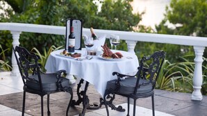 A table set for two with a white tablecloth, two black chairs, a bottle of wine, glasses, and a lobster on the table. - Jamaica Palace Hotel (Port Antonio)