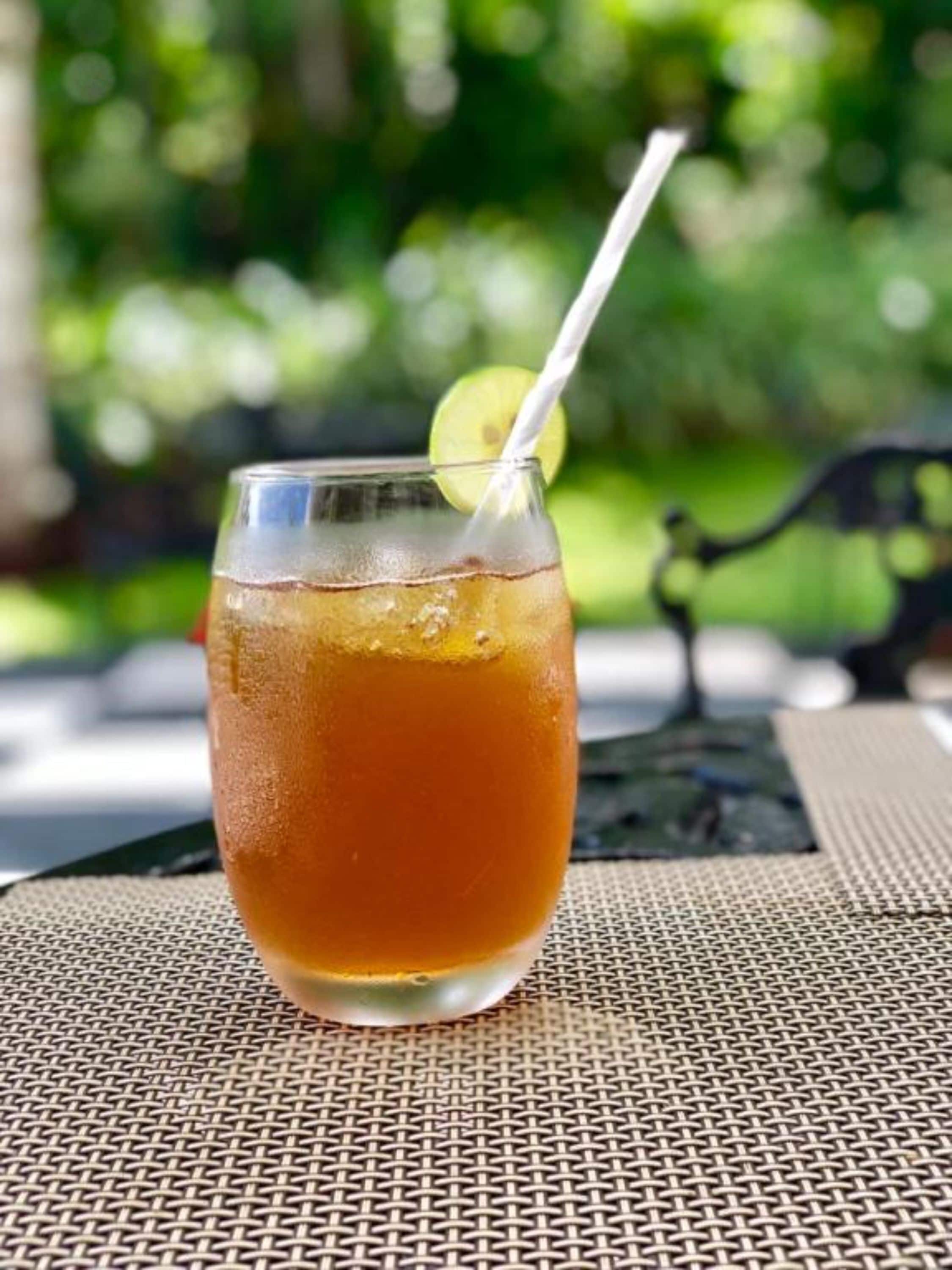 Un verre de thé glacé avec une paille et une tranche de citron vert, posé sur un set de table en fibres tressées.
