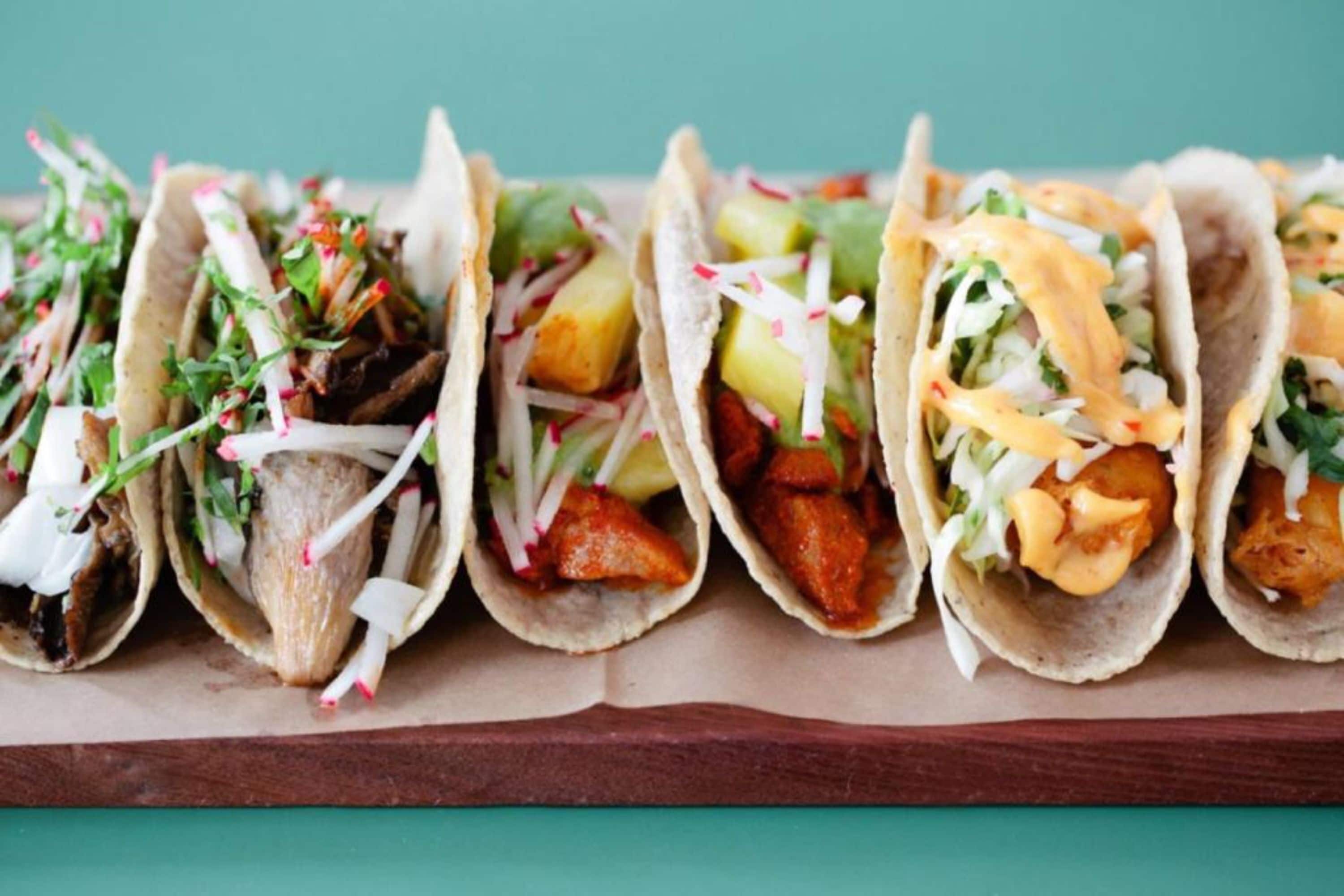 A row of tacos with various fillings and toppings.