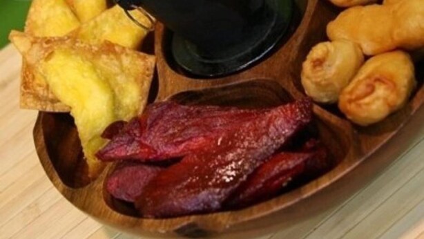 Een houten dienblad met diverse gebakken gerechten, waaronder gebakken vis, aardappelpartjes en een stuk vlees.