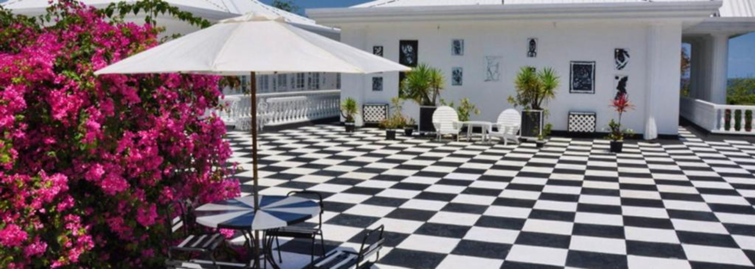 A checkered outdoor patio with white chairs and tables, surrounded by white walls and pink bougainvillea flowers.