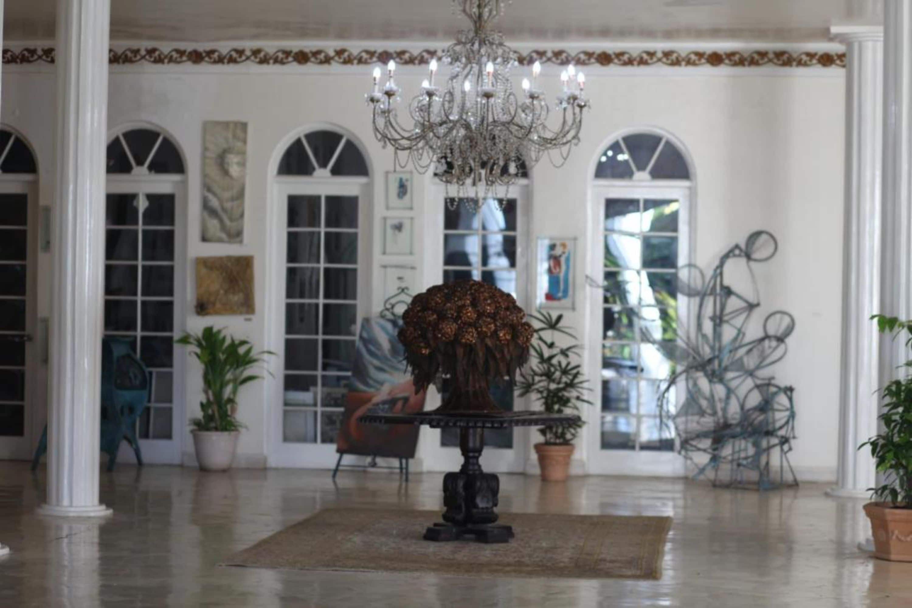 A spacious lobby with a chandelier, potted plants, and a large vase of flowers on a table.