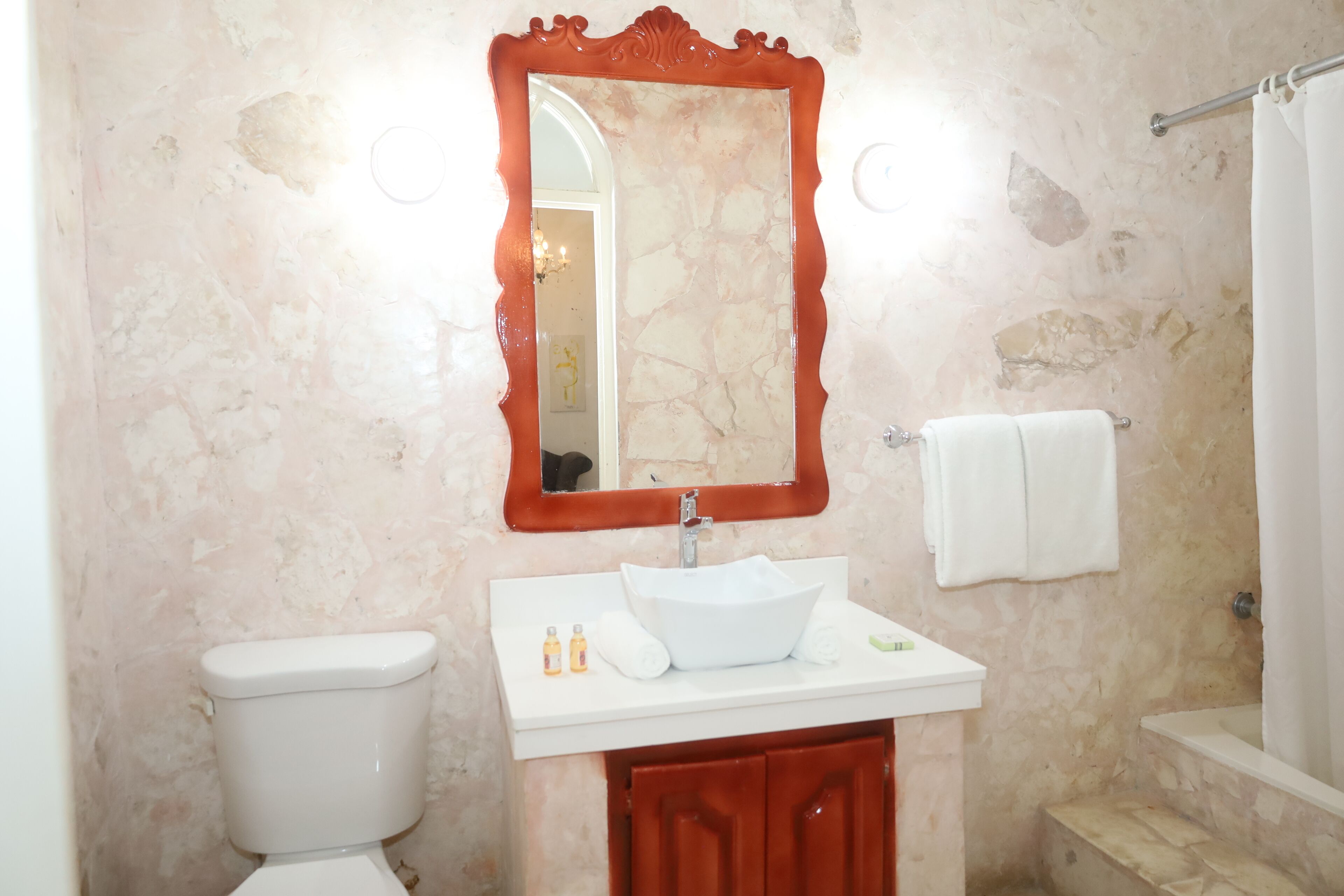 A bathroom with a white sink, a mirror with a red frame, a toilet, and a shower area.