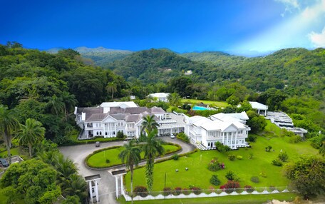 A large, white, colonial-style hotel with multiple buildings, surrounded by lush greenery and hills.