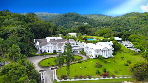 A large, white, colonial-style hotel with multiple buildings, surrounded by lush greenery and hills. - Jamaica Palace Hotel (Port Antonio)