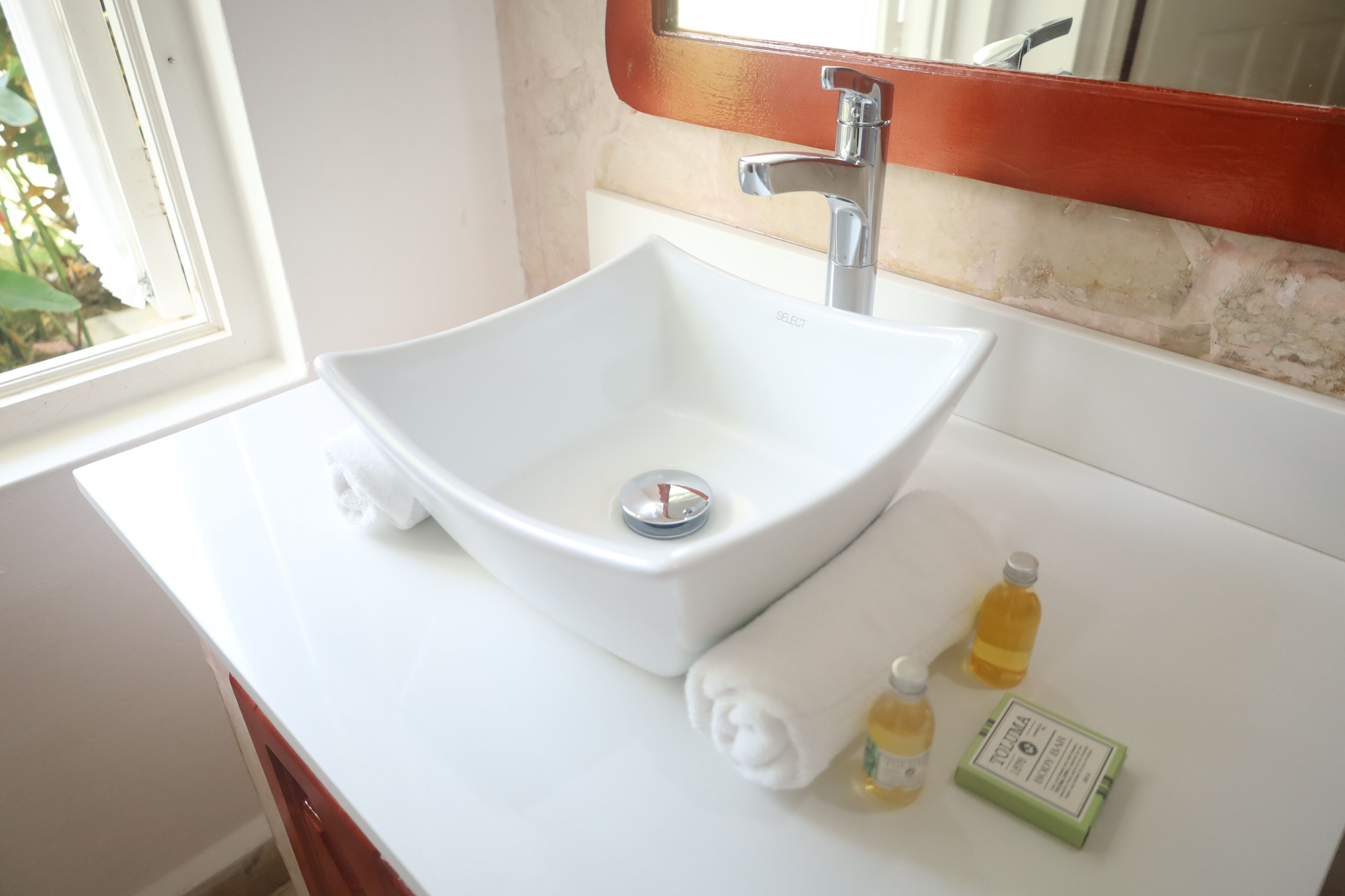 A white bathroom sink with a modern faucet, a towel, and two bottles of lotion on the countertop.