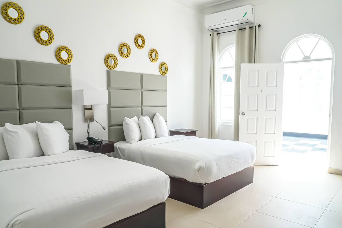 Une chambre d’hôtel avec deux lits, une table de chevet avec une lampe, un climatiseur fixé au mur et des éléments décoratifs circulaires accrochés au mur.