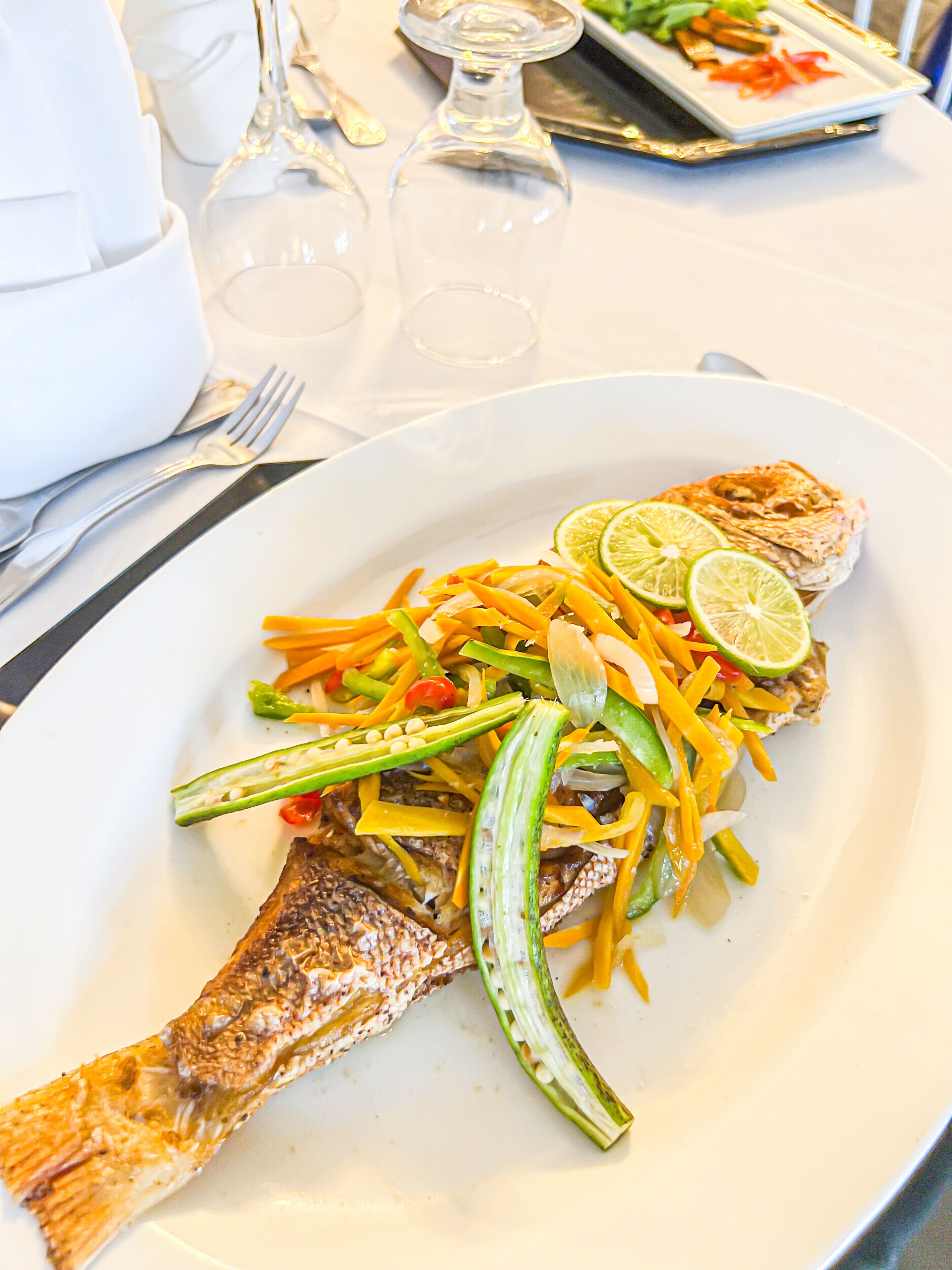 Une assiette contenant un poisson grillé, garni de légumes et de tranches de citron vert.