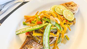 Une assiette contenant un poisson grillé, garni de légumes et de tranches de citron vert.