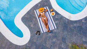 A woman lying on a striped towel by a pool with a hat, a plate of fruit, and a pair of flip-flops. - Jamaica Palace Hotel (Port Antonio)