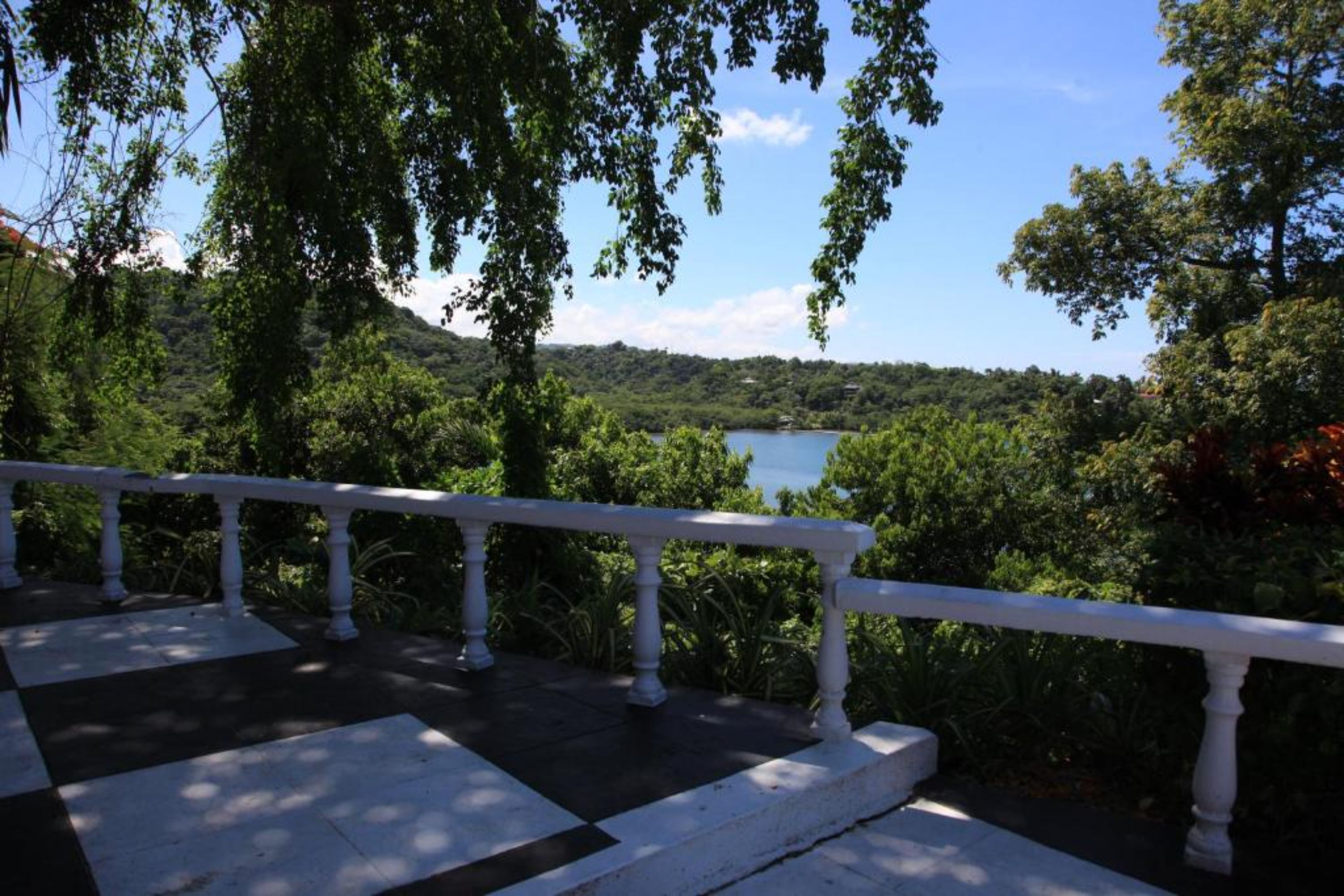 Un balcon doté d’une balustrade blanche, donnant sur un lac bordé d’une végétation luxuriante.
